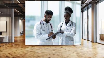 Two doctors: indian male and african female discussing test reports that show on their clipboard Wall mural